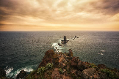 Rocky headland at Cape Kamui with offshore sea stack under warm evening light in Hokkaido, Japan.