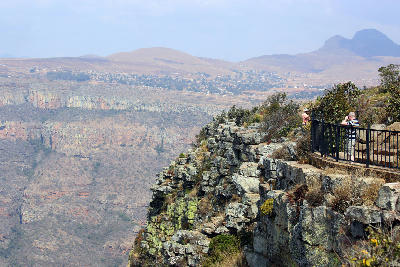 Visitor standing at a cliff-edge viewpoint overlooking the Blyde River Canyon escarpment and surrounding mountain landscape in Mpumalanga, South Africa.