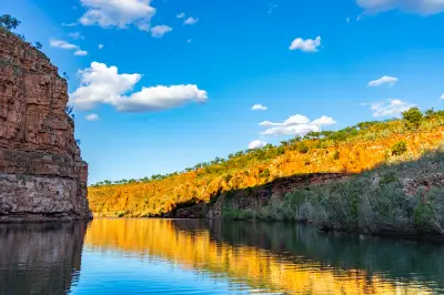 Golden sunlight illuminates the sandstone cliffs of Chamberlain Gorge, reflected in the calm waters of the Chamberlain River.