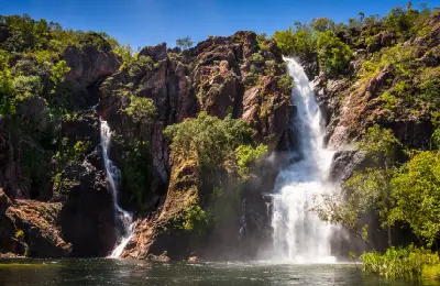Two waterfalls cascading down rugged sandstone cliffs into a large plunge pool at Wangi Falls during the wet season in Litchfield National Park, Australia.