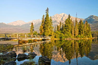 Wooden bridge to a forested island reflected in calm Pyramid Lake with mountains behind