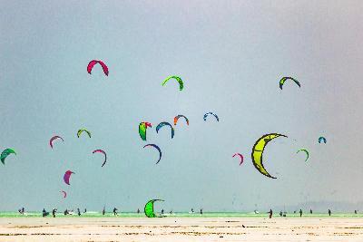 Colourful kites flying above kitesurfers on the shallow lagoon at Paje Beach, Zanzibar, Tanzania.