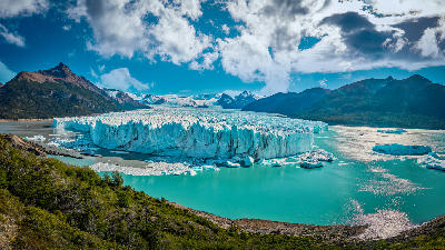 Perito Moreno Glacier with blue ice wall and turquoise lake surrounded by mountains in Patagonia, Argentina.