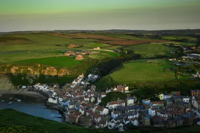 Elevated view of Staithes fishing village, showing red-roofed cottages clustered around the harbour beneath rolling green hills in North Yorkshire.