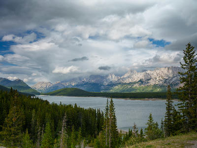 Mountain lake in Peter Lougheed Provincial Park surrounded by evergreen forest and rugged Rocky Mountain peaks under dramatic cloud cover, Alberta, Canada.