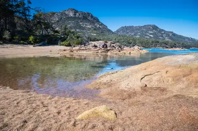 Red granite shoreline and clear water at Honeymoon Bay beneath The Hazards, Freycinet National Park, Tasmania.
