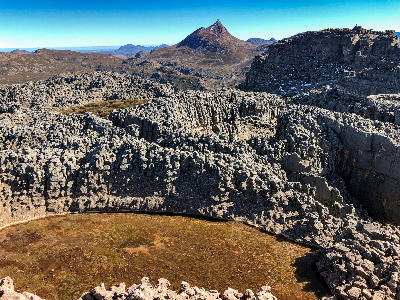 View from Luna Peak across the high sandstone plateau of the southern Cederberg, with rugged rock formations, a small mountain tarn, and Sneeuberg Peak rising in the distance.