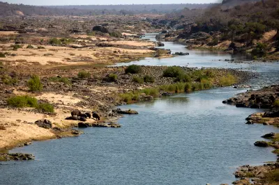 Panoramic view of the Olifants River from N'wamanzi Lookout in Kruger National Park, showing rocky riverbanks, sandbars and wilderness vegetation stretching into the distance.