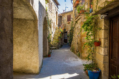 Sunlit medieval alley with stone steps and houses in the historic centre of Pitigliano, Tuscany, Italy.