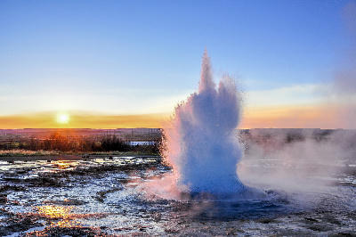 Geysir erupting at sunset in the Golden Circle, Iceland, with steam plume rising from geothermal pool