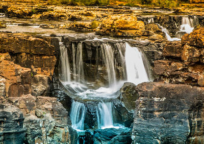 Water cascading over layered rock formations at Bourke's Luck Potholes in Mpumalanga, South Africa.