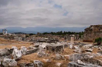 Scattered stone columns, foundations, and architectural fragments of the ancient Nymphaeum complex at Hierapolis, with mountains in the distance.