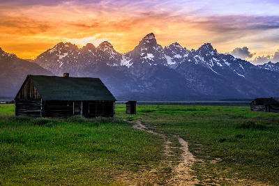 Historic cabins on Mormon Row with the Teton Range silhouetted against sunset sky, Grand Teton National Park, Wyoming, USA.