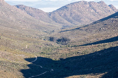 Panoramic view across the Cederberg Mountains with Algeria visible in the valley below and the winding Nieuwoudt Pass descending through rugged sandstone landscapes in the Western Cape, South Africa.