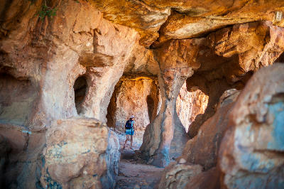 Woman exploring a maze-like sandstone cave at Truitjieskraal in the Cederberg Wilderness Area, surrounded by sculpted rock chambers, natural arches, and weathered sandstone formations in the Western Cape, South Africa.