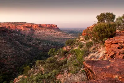 Soft dawn light illuminates the red sandstone cliffs and rugged valley of Kings Canyon beneath a pink sky.