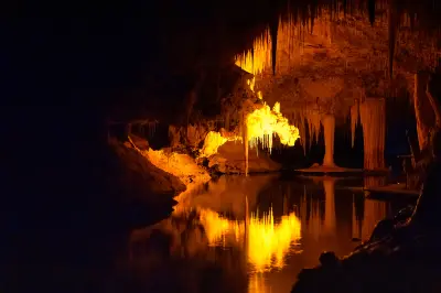Illuminated stalactites and limestone formations reflected in the underground lake at Lake Cave, Western Australia.