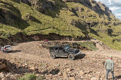 Four-wheel-drive vehicles driving around a steep gravel hairpin bend on Sani Pass in the Drakensberg mountains.