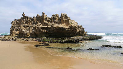 Castle Rock sandstone formation on Brenton-on-Sea Beach with tidal pools, golden sand and ocean waves near Knysna, South Africa.
