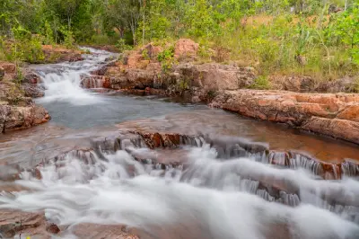 Cascading white water flowing over reddish sandstone ledges between natural swimming pools at Buley Rockhole, Litchfield National Park, Northern Territory, Australia.