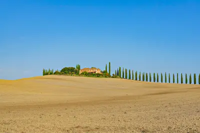 Poggio Covili farmhouse with a long row of cypress trees on a ridge in the Tuscan countryside near Montalcino.