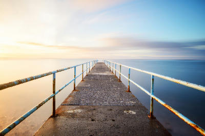Concrete pier with metal railings extending into the Atlantic Ocean at sunset in Santa Cruz, Madeira Island, Portugal.
