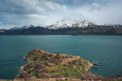 Aerial view of Akdamar Island and the Cathedral of the Holy Cross in Lake Van with snow-covered mountains in the background.