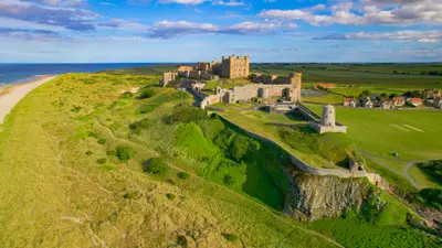 Aerial view of Bamburgh Castle perched above the North Sea coastline, showing its medieval fortifications, surrounding dunes, sandy beach and Bamburgh village in Northumberland, England.