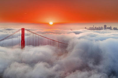 Golden Gate Bridge emerging above fog at sunrise with San Francisco skyline in background