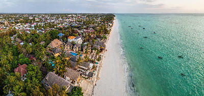 Drone view of Paje Beach showing white sand, turquoise water, beachfront resorts, palm trees and traditional fishing boats in Zanzibar, Tanzania.
