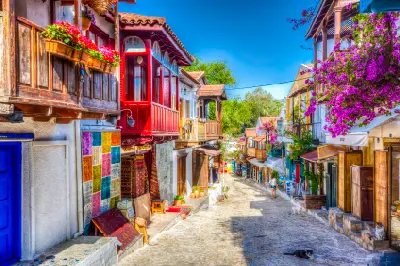 Cobbled street in historic Kaş lined with traditional wooden balconies, colorful façades, bougainvillea and small shops.