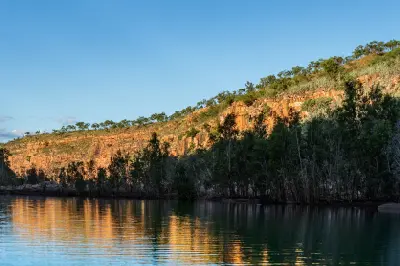 Warm sunlight catches the upper sandstone cliffs of Chamberlain Gorge while the Chamberlain River and riverside vegetation remain in deep shade.