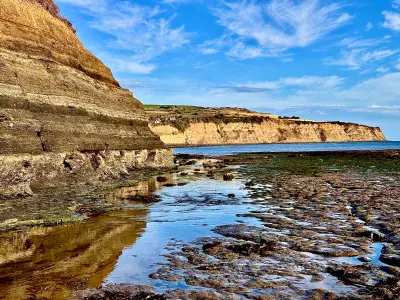 Sandstone cliffs and rocky tidal pools at Robin Hood's Bay in North Yorkshire, with reflections in shallow water and distant coastal headlands.