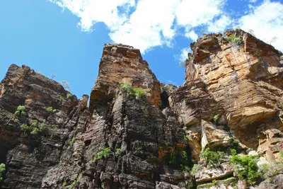 Low-angle view of towering orange and dark layered sandstone cliffs at Jim Jim Falls in Kakadu National Park, Northern Territory, Australia.