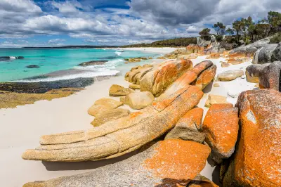 Orange-lichen granite boulders, white sand and turquoise water along the Bay of Fires coastline in northeast Tasmania.