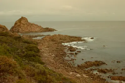 Sugarloaf Rock beside a rugged granite shoreline and coastal vegetation at Cape Naturaliste in Western Australia.