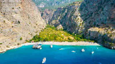 Aerial view of Butterfly Valley showing the turquoise bay, beach, boats and steep surrounding cliffs near Ölüdeniz, Türkiye.