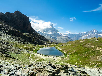 Riffelsee lake with hikers on surrounding trails and Matterhorn partially covered by clouds, Zermatt, Switzerland.