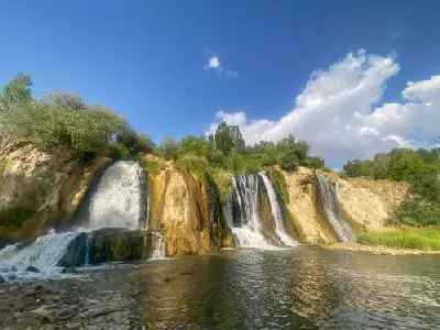 Muradiye Waterfall cascading over rocky cliffs into a broad pool surrounded by green vegetation in Van Province, Turkey.