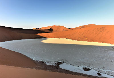 Curved white clay pan enclosed by red sand dunes in Hiddenvlei, Namibia’s Namib Desert.