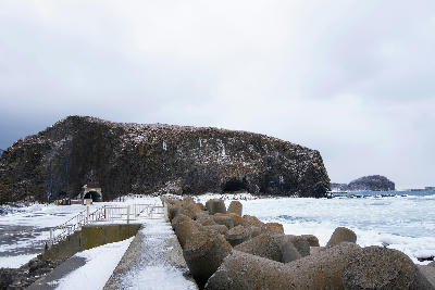 Olonko Rock in winter with snow-covered breakwater and sea ice at Utoro, Shiretoko, Hokkaido