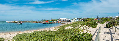Panoramic view of Struisbaai Harbour with fishing boats, coastal dunes, and seaside buildings beneath blue skies in the Western Cape.