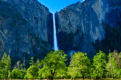 Bridalveil Fall Yosemite with tall waterfall against granite cliff and green trees across the valley foreground.