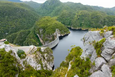 Wide aerial view of Gordon Dam and Lake Gordon among rugged forested mountains in southwest Tasmania, Australia.