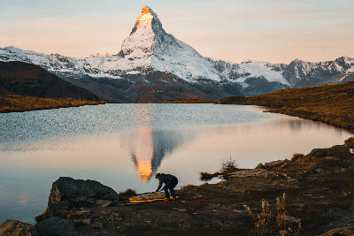 Matterhorn reflected in Stellisee at sunrise with person on the lakeshore, Zermatt, Switzerland.