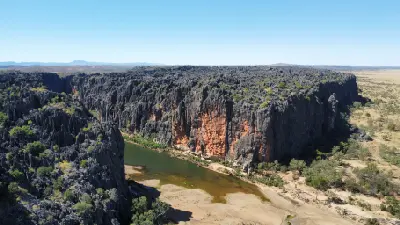 Aerial view of the Lennard River winding beneath towering dark limestone walls streaked with orange at Bandilngan (Windjana Gorge).