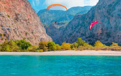 Paragliders flying between the towering cliffs of Butterfly Valley above turquoise water near Ölüdeniz, Türkiye.