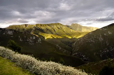 Sunlit ridges of the Outeniqua Mountains rising above deep valleys beneath dramatic storm clouds in the Garden Route region of South Africa.