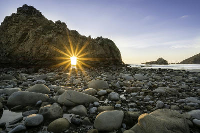 Sunstar through rock arch at Pfeiffer Beach Big Sur California coastline