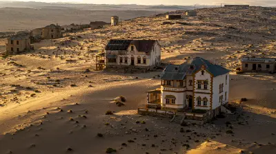 Aerial view of abandoned colonial-era buildings partially buried by windblown sand at Kolmanskop near Lüderitz, Namibia, with desert dunes stretching across the surrounding landscape.